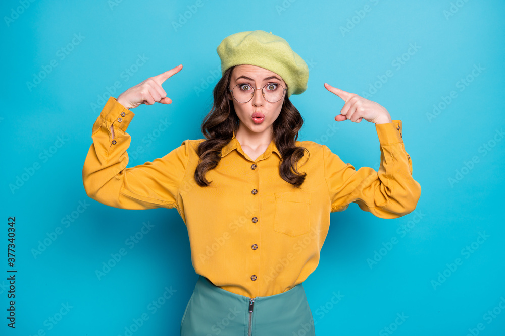 Portrait of astonished girl point index finger her cap dont like look isolated over blue color background Portrait of astonished girl point index finger her cap dont like look isolated over blue color background