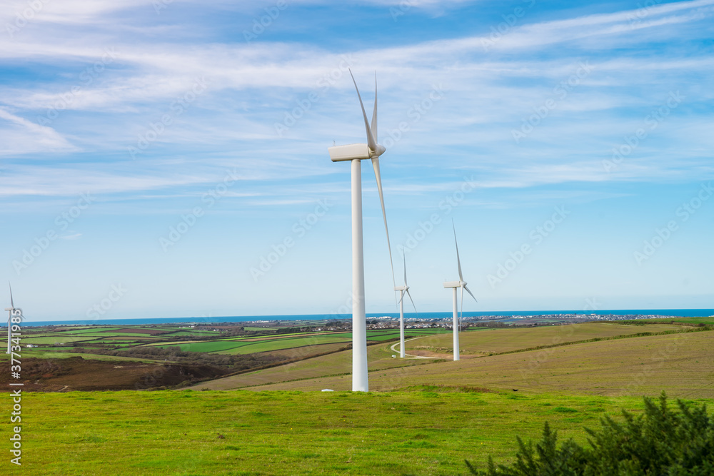 Wind turbine - renewable energy source on green meadows with sea on horizon. The concept of environmental protection and friendly use. Modern equipment for generating electric energy. Modern windmills Wind turbine - renewable energy source on green meadows with sea on horizon. The concept of environmental protection and friendly use. Modern equipment for generating electric energy. Modern windmills