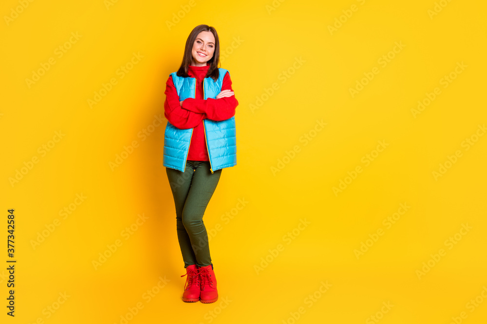 Full length photo of cute lovely young lady smiling folded hands self-assured look waiting skiing time wear green pants blue vest red sweater boots isolated bright yellow color background