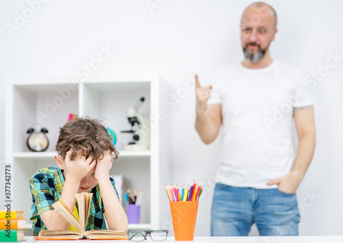 Angry father scolds his son for poor study photo