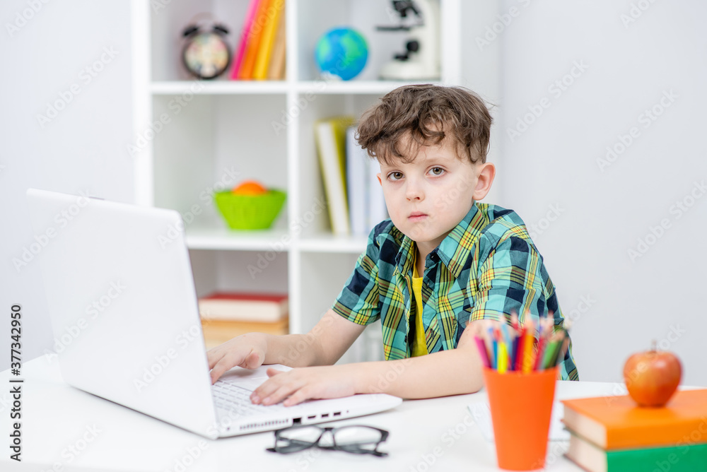 Serious boy uses laptop at home. Distance learning concept