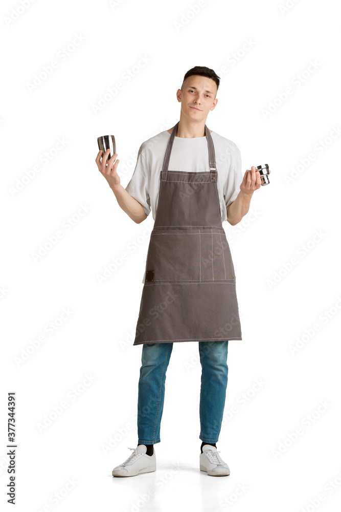 Shaker. Portrait of a young male caucasian barista or bartender in brown apron smiling. Studio white background, copyspace. Holding cocktails, inviting guests. Professional occupation, drink, service. Shaker. Portrait of a young male caucasian barista or bartender in brown apron smiling. Studio white background, copyspace. Holding cocktails, inviting guests. Professional occupation, drink, service.