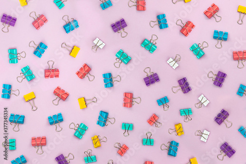 Multi-colored binder clips scattered over a pink background