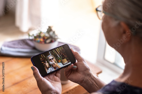 Defocused senior woman using smart phone to video call with sister absent due to coronavirus - on the screen smiling lady takes off the mask doing ok sign with hand
