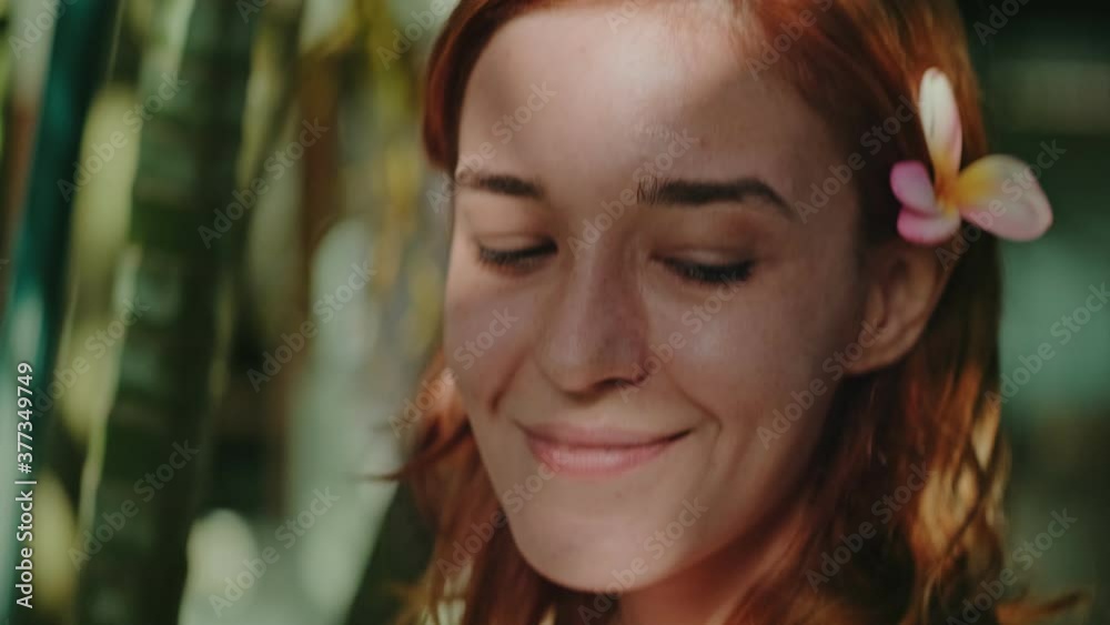 Young redhead woman posing in the bamboo forest, smiling looking at the camera, has a frangipani flower in her hair above ear. Travel, retreat, yoga and meditation concept Young redhead woman posing in the bamboo forest, smiling looking at the camera, has a frangipani flower in her hair above ear. Travel, retreat, yoga and meditation concept