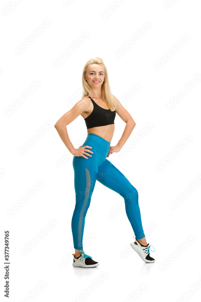 Smiling. Beautiful female fitness coach practicing isolated on white studio background, showing exercises. Caucasian blonde model in sport outfit. Professional occupation, active and healthy lifestyle