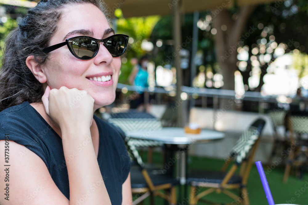 Young woman wearing sunglasses, smiling, waiting, sitting in an outdoor bar. Young woman wearing sunglasses, smiling, waiting, sitting in an outdoor bar.