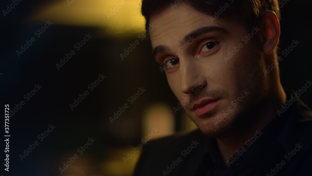 Charming guy raising eyebrows in dark background. Handsome man smiling indoors. Charming guy raising eyebrows in dark background. Handsome man smiling indoors.