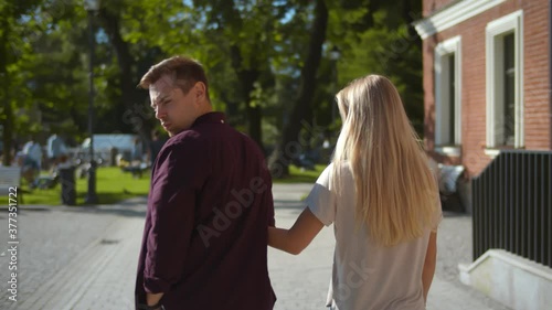 Back view of young man walking with girlfriend and looking at another woman passing by photo