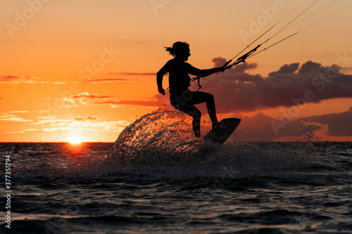 Silhouette of kitesurfer jumping with spray water in beautiful orange sunset conditions