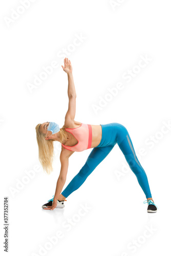 Beautiful female fitness coach practicing isolated on white studio background. Caucasian blonde model working in sport outfit and face mask. Professional occupation, active and healthy lifestyle.