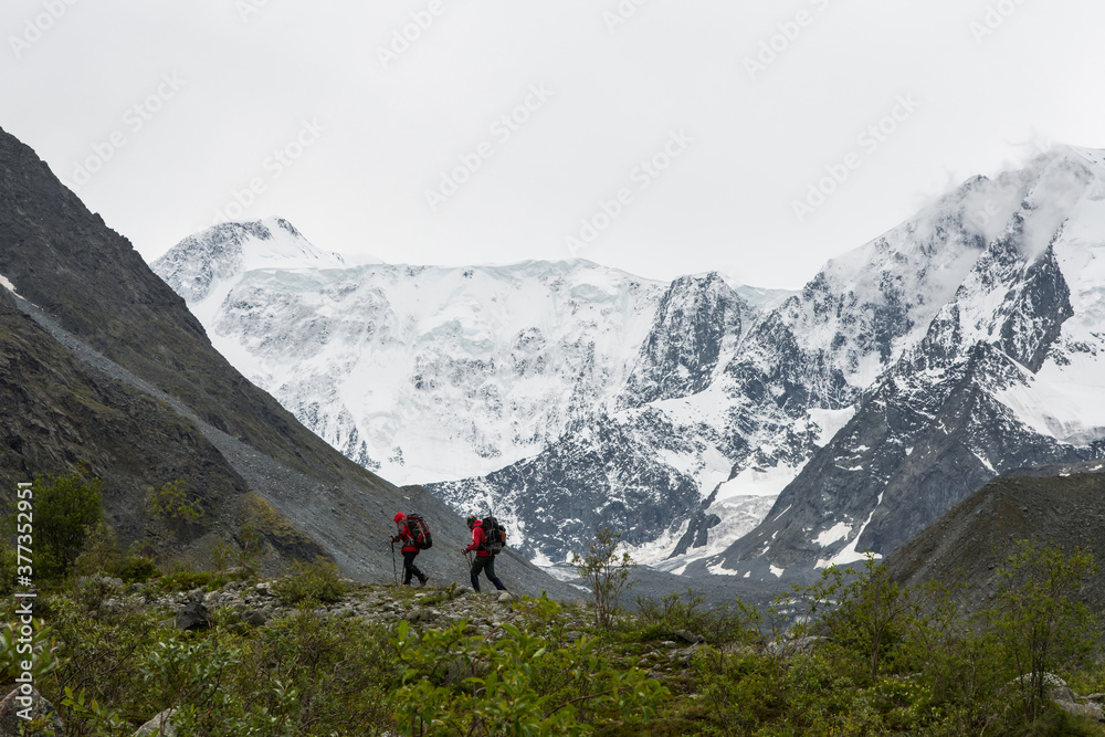 two climbers walk along the crest of the mountain against the background of the snow-capped peaks of 