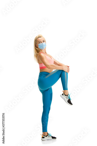Beautiful female fitness coach practicing isolated on white studio background. Caucasian blonde model working in sport outfit and face mask. Professional occupation, active and healthy lifestyle.