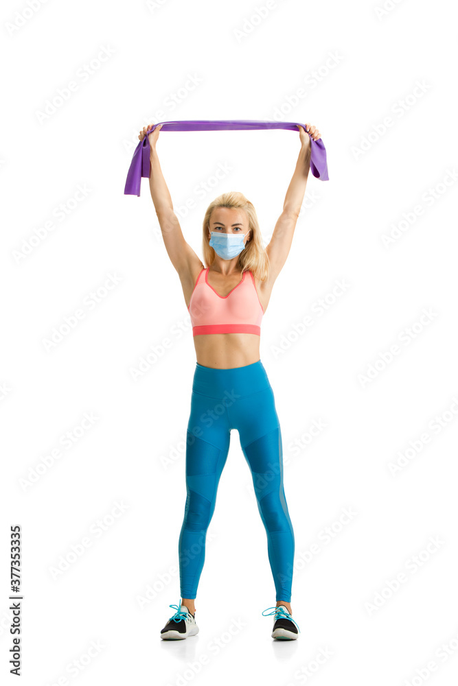 Beautiful female fitness coach practicing isolated on white studio background. Caucasian blonde model working in sport outfit and face mask. Professional occupation, active and healthy lifestyle.