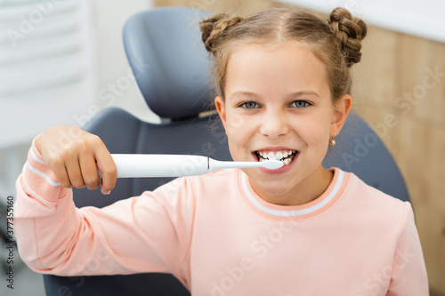 Pretty little girl cleaning teeth with electric sonic toothbrush. Perfect removing plaque with a modern toothbrush photo