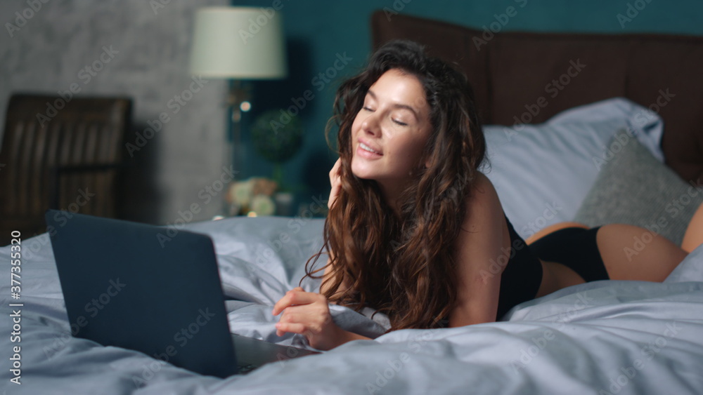 Charming woman having fun with laptop bed. Sensual girl using computer indoors