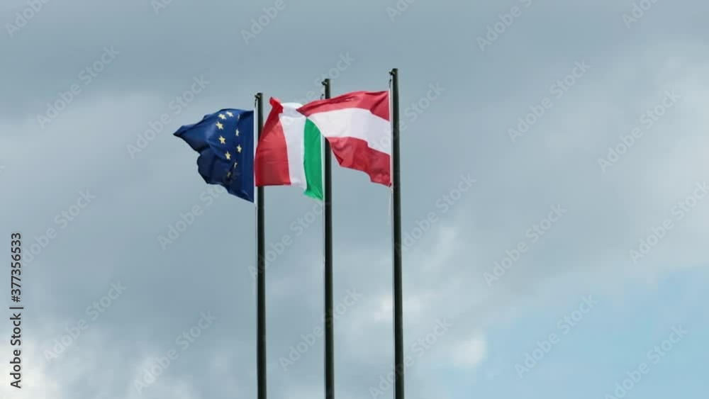 Austrian, italian and European flag blowing in the wind of a cloudy day Austrian, italian and European flag blowing in the wind of a cloudy day