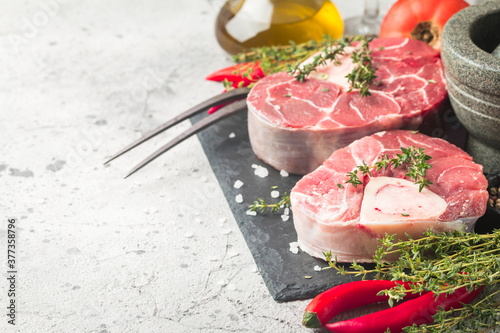 Fresh veal shank slices beef meat for Osso Buco cooking on cutting board with ingredients and seasonings thyme, pepper, salt.
