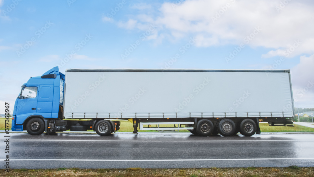 Side View Shot of a Blue Long Haul Semi-Truck with Cargo Trailer Attached Stopped on a Road in the Rural Area. Logistics Company Moving Goods Across Countrie Continent.