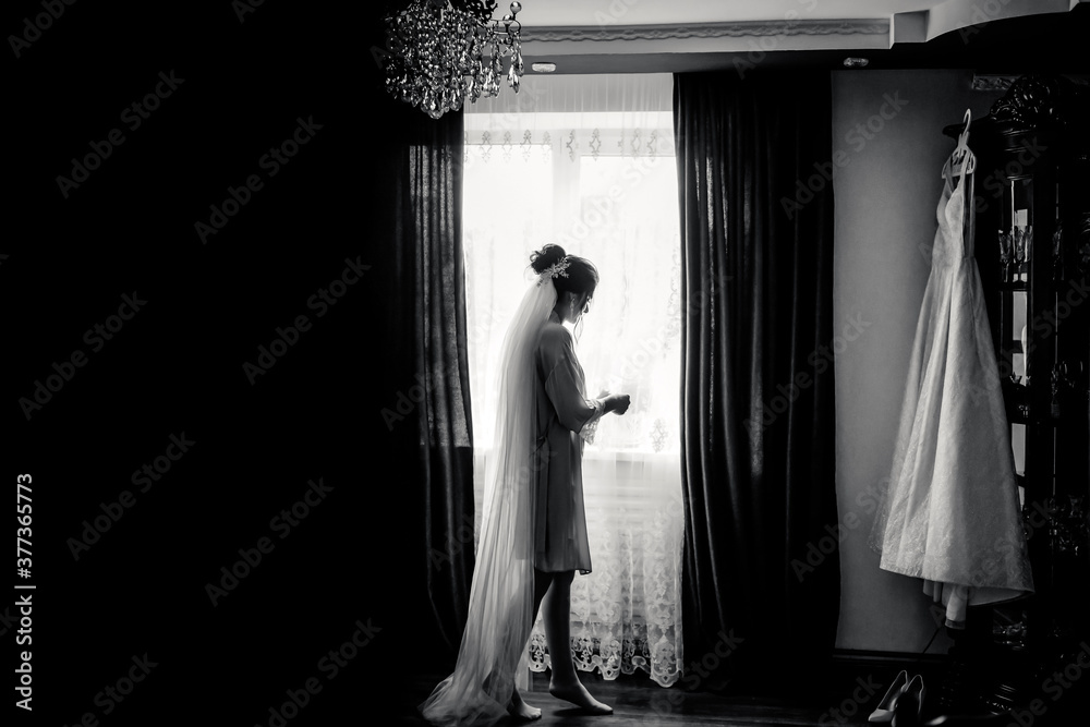 Black and white photo beautiful bride in a dressing gown poses near window