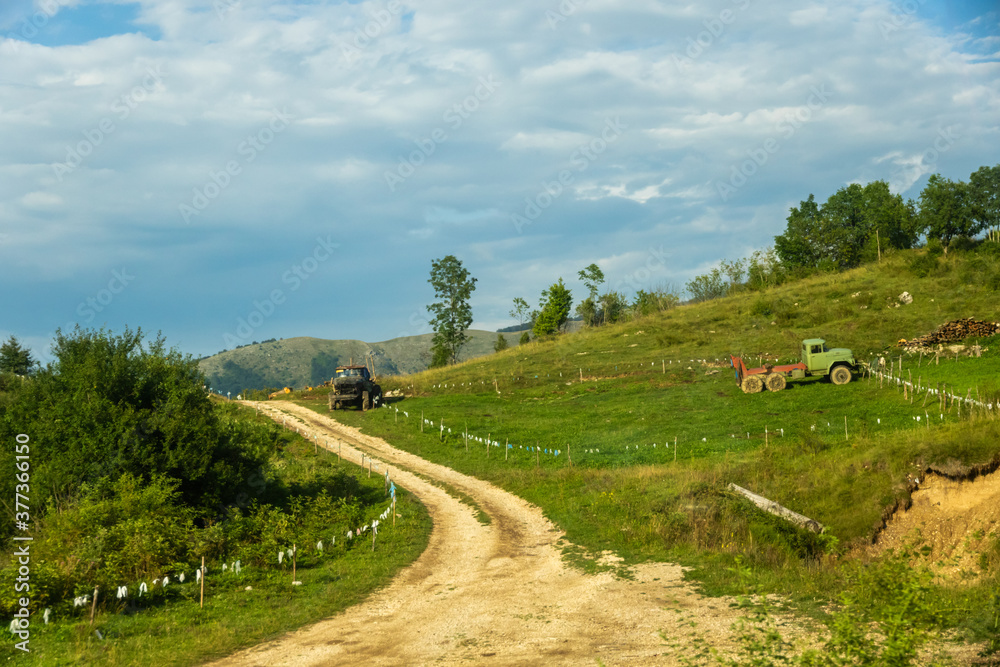 Country road with a tractor in the mountains and on the horizon of high peaks