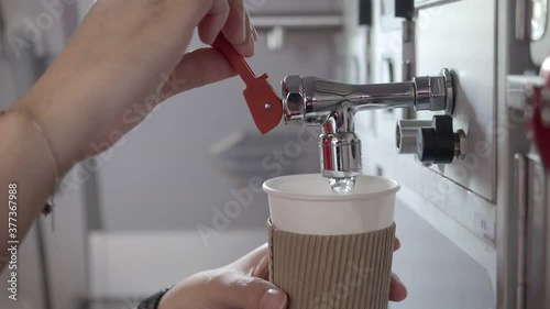 female cabin crew pouring hot water into paper cup covered with cup sleeve in aircraft aft galley.