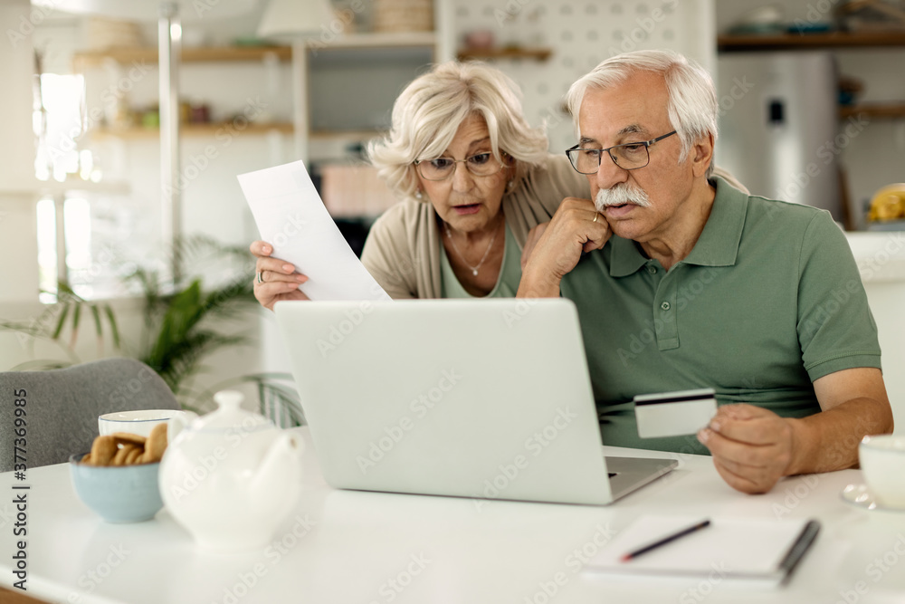 Distraught senior couple e-banking with credit card and laptop at home. Distraught senior couple e-banking with credit card and laptop at home.