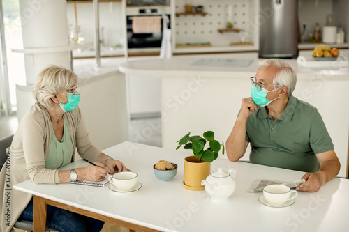 Fototapeta Naklejka Na Ścianę i Meble -  Senior couple with face masks talking while sitting at the table at home.