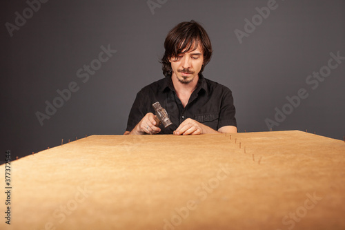 A man hammers nails into a cupboard. The back wall of the cupboard is made of thick cardboard. photo