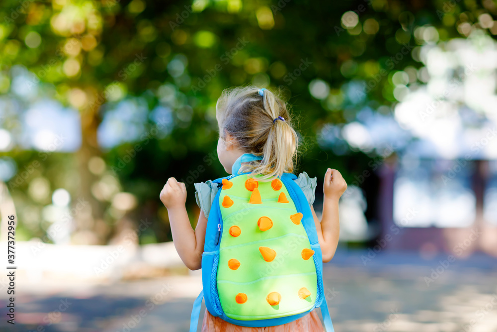 Naklejka premium Cute little adorable toddler girl on her first day going to playschool. Healthy beautiful baby walking to nursery preschool and kindergarten. Happy child with backpack on the city street, outdoors.
