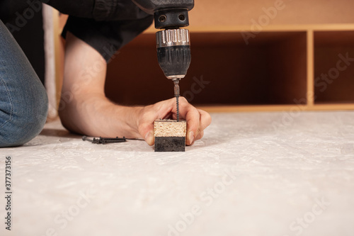 A man drills a hole in the wood against the background of an inverted closet on the floor.