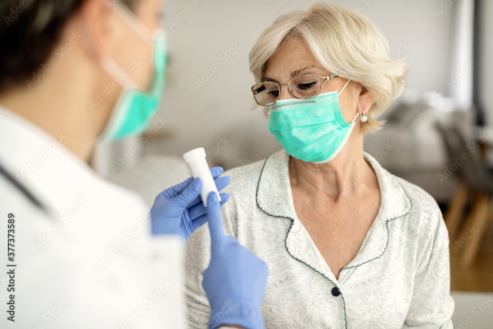 Mature woman wearing protective face mask while getting pills from a doctor during home visit. Mature woman wearing protective face mask while getting pills from a doctor during home visit.
