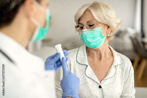 Mature woman wearing protective face mask while getting pills from a doctor during home visit.