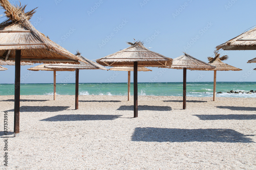 Straw umbrellas at empty beach on summer day