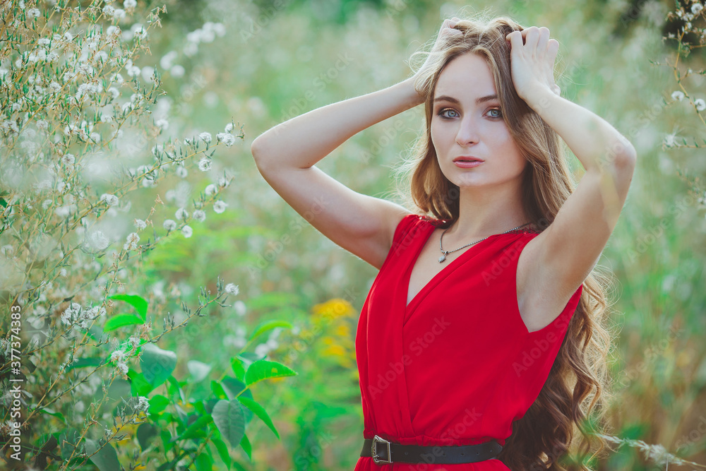 Portrait of a young beautiful girl in a red dress on the summer field outdoors