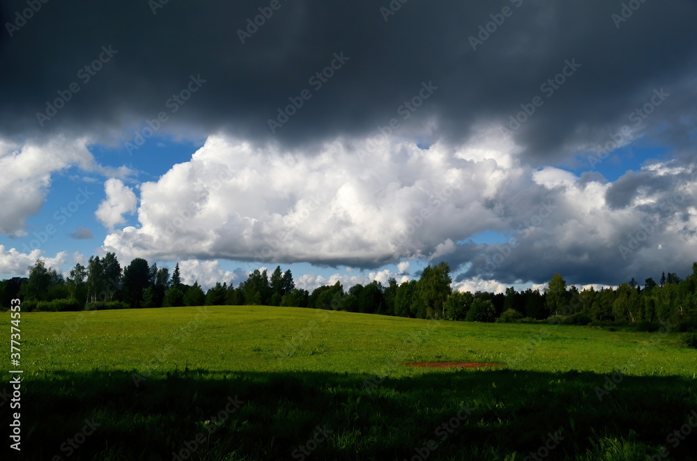 Black storm clouds during summer, Landscape with trees and meadows in the foreground in Latvia. Low clouds Black storm clouds during summer, Landscape with trees and meadows in the foreground in Latvia. Low clouds