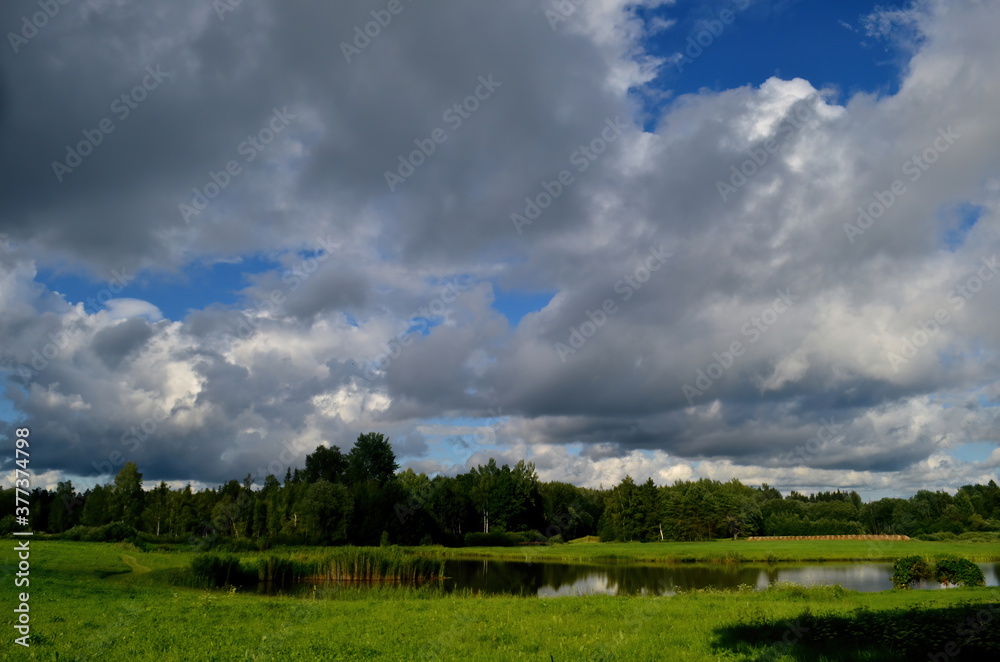 Black storm clouds during summer, Landscape with trees and meadows in the foreground in Latvia. Low clouds Black storm clouds during summer, Landscape with trees and meadows in the foreground in Latvia. Low clouds