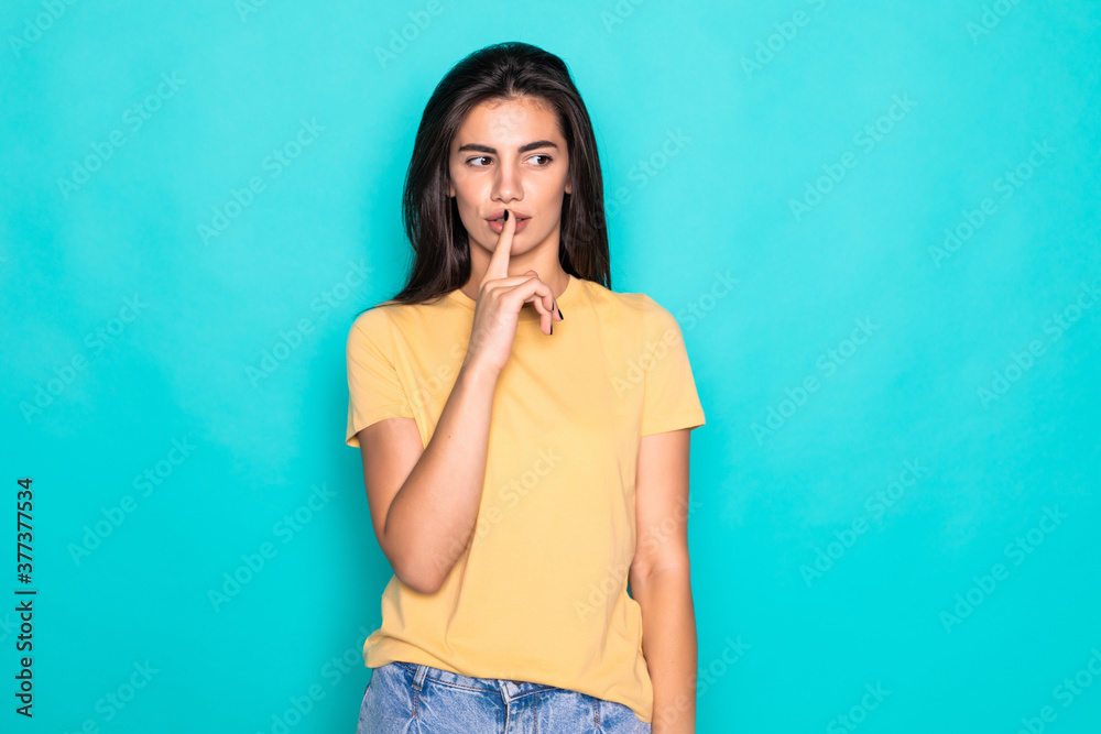 Portrait of cute sweet woman holding forefinger near lips isolated on turquoise background Portrait of cute sweet woman holding forefinger near lips isolated on turquoise background