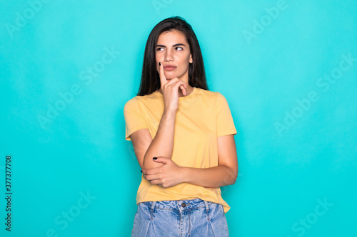 Beautiful young woman holding hand on chin on turquoise background.