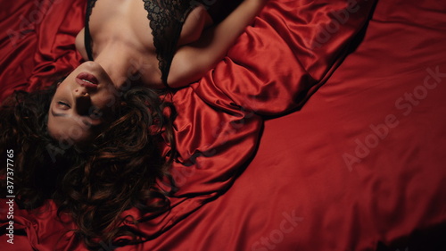 Sexy girl looking camera on red silk bed. Charming woman relaxing satin sheets.