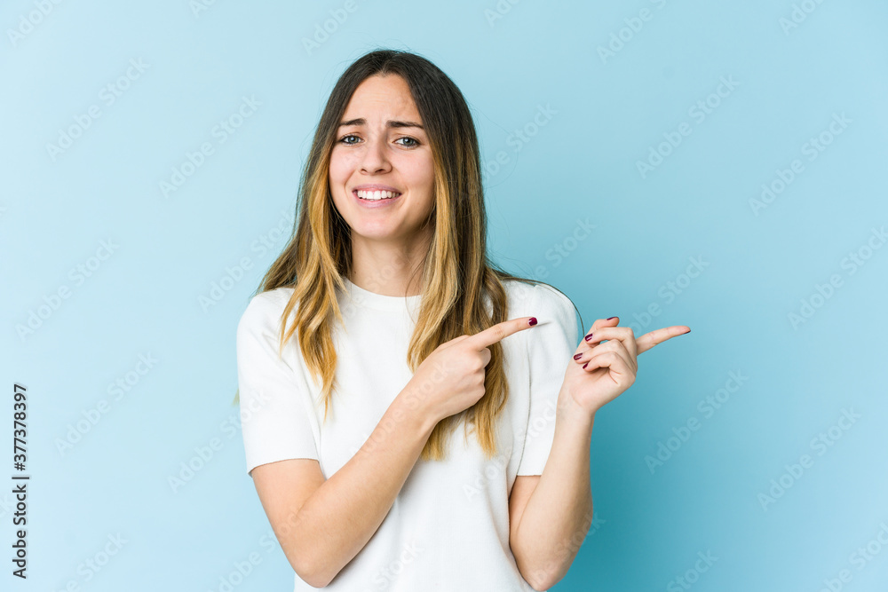 Young caucasian woman isolated on blue background shocked pointing with index fingers to a copy space. Young caucasian woman isolated on blue background shocked pointing with index fingers to a copy space.