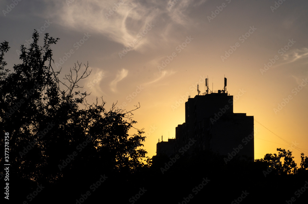 The sun sets behind a building against the sky