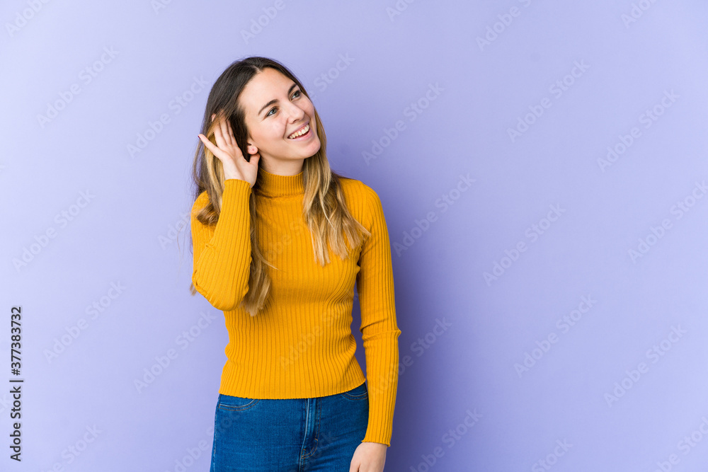Young caucasian woman isolated on purple background trying to listening a gossip. Young caucasian woman isolated on purple background trying to listening a gossip.