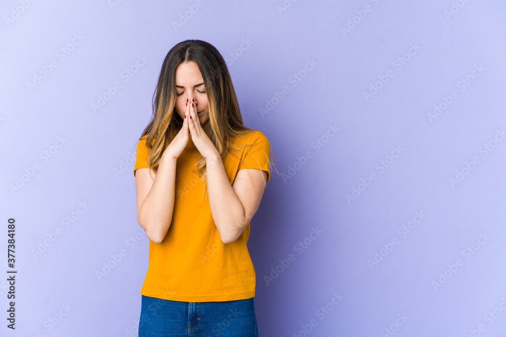 Young caucasian woman isolated on purple background praying, showing devotion, religious person looking for divine inspiration. Young caucasian woman isolated on purple background praying, showing devotion, religious person looking for divine inspiration.