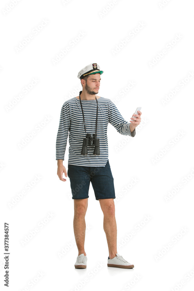 Scrolling phone. Caucasian male sailor in uniform on white studio background. Young man using modern devices and gadgets in his work. Concept of tech, professional occupation, job of seaman. Scrolling phone. Caucasian male sailor in uniform on white studio background. Young man using modern devices and gadgets in his work. Concept of tech, professional occupation, job of seaman.