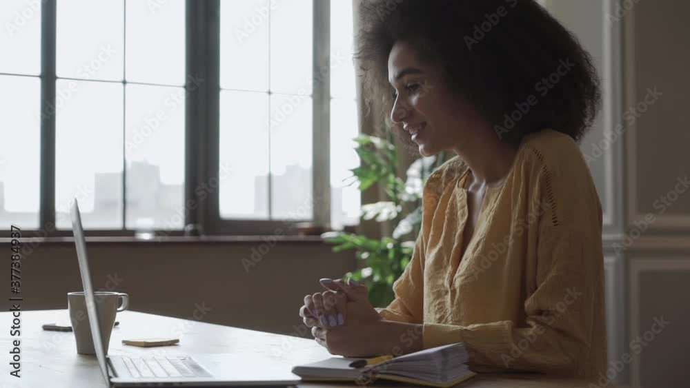 Cute smiling young african american teen girl video calling on laptop. Happy mixed race pretty woman student looking at computer screen studying remotely. Cute smiling young african american teen girl video calling on laptop. Happy mixed race pretty woman student looking at computer screen studying remotely.