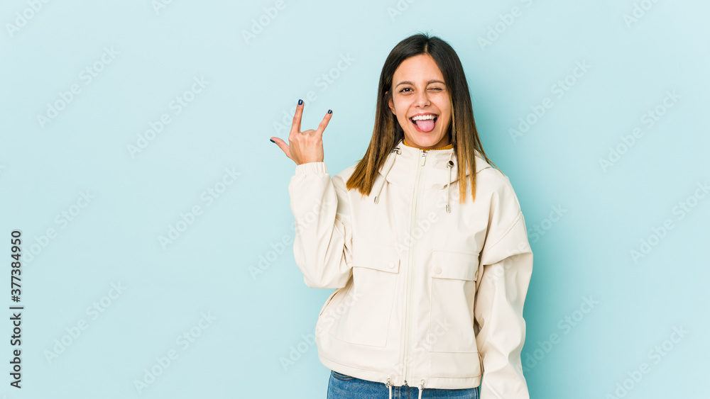 Young woman isolated on blue background showing rock gesture with fingers Young woman isolated on blue background showing rock gesture with fingers