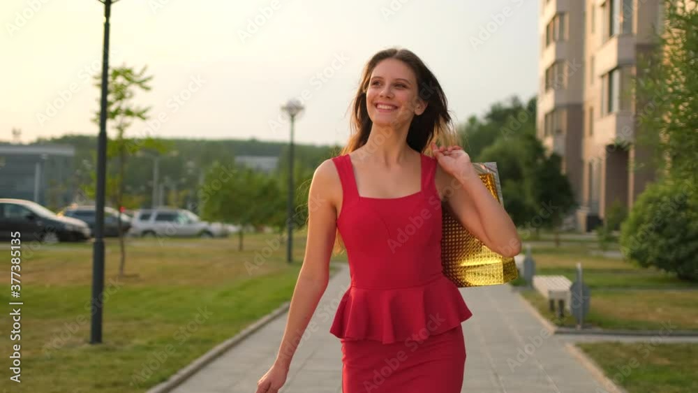 Stylish smiling beautiful young shopping girl woman female in red dress with bags packages walking outdoors street city. Shop, mall, fashion, shopper, shopaholic, shopping center concept. 4 K slow-mo Stylish smiling beautiful young shopping girl woman female in red dress with bags packages walking outdoors street city. Shop, mall, fashion, shopper, shopaholic, shopping center concept. 4 K slow-mo