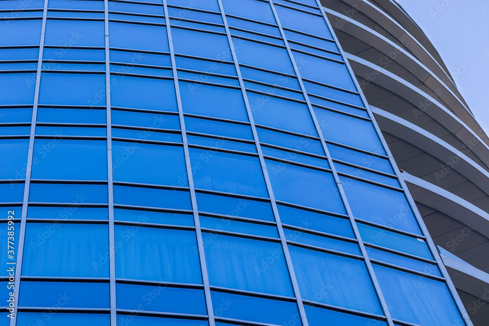 Obraz premium The bright blue sky is reflected in the windows of a modern glass building. Abstract fragment of a modern building. Sunny day.