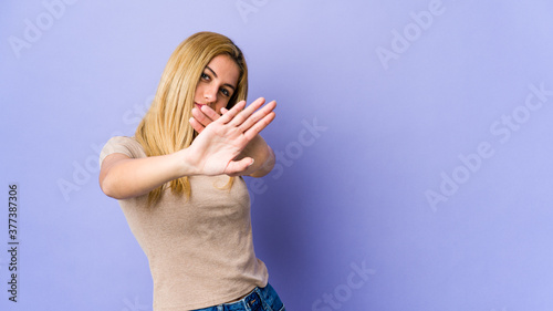 Young blonde woman isolated on purple background standing with outstretched hand showing stop sign, preventing you.